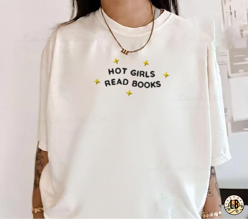 K&ouml;nnte beinhalten: Cremefarbenes T-Shirt mit dem schwarzen Schriftzug "HOT GIRLS READ BOOKS", umgeben von gelben Sternen. Das kurz&auml;rmlige Shirt hat eine lockere Passform und eignet sich f&uuml;r Freizeitkleidung.