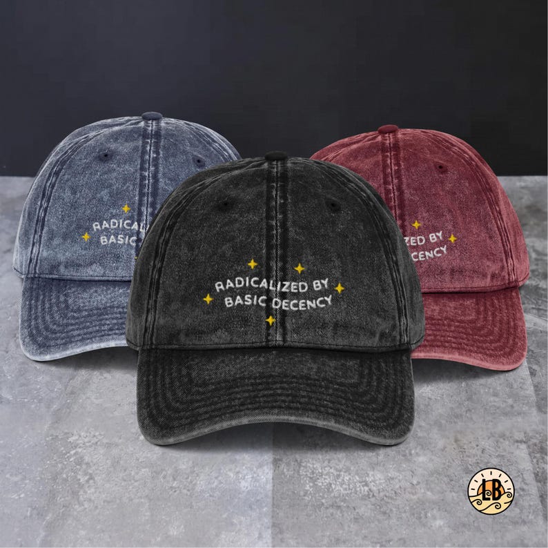 Op de afbeelding: Drie baseballpetten in acid-washed blauw, zwart en bordeauxrood. Elke pet is voorzien van de geborduurde witte tekst "RADICALIZED BY BASIC DECENCY" in het midden aan de voorzijde, geaccentueerd door kleine gele vierpuntige sterren.