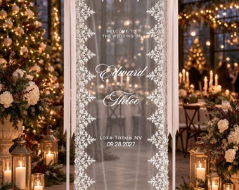 Könnte beinhalten: Ein hohes, rechteckiges Hochzeits-Willkommensschild aus einem transparenten weißen Stoff mit aufwendigen weißen Spitzenrändern. Das Schild zeigt den Text: WELCOME TO THE WEDDING OF Edward + Chloe Lake, Tahoe, NV 09.28.2027, verziert mit zwei hellrosa Schleifen.