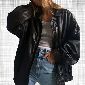 Könnte beinhalten: Eine schwarze Lederjacke mit Kragen und Reißverschluss. Die Jacke hat lange Ärmel mit geknöpften Manschetten und einen gerippten Saum. Das Model trägt ein weißes Tanktop und blaue Jeans.