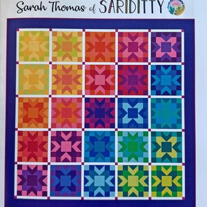May include: A Waypoint quilt pattern by Sarah Thomas of Sariditty featuring a 5x5 grid of colorful star blocks in a rainbow gradient. The finished size is 74 inches by 74 inches. The design includes white sashing and cornerstones between blocks.