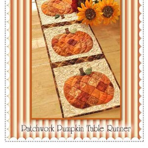 May include: A patchwork pumpkin table runner with five orange pumpkins in a row. The pumpkins are made of different fabrics and have a quilted look. The table runner is on a wood floor and there are some fall flowers in the background. The text "Shabby Fabrics" is at the top of the image and the text "Patchwork Pumpkin Table Runner" is at the bottom.