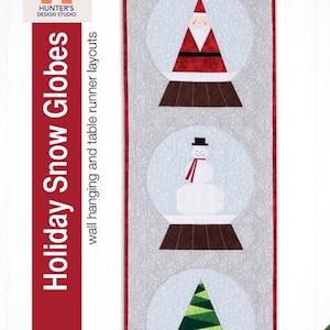 May include: A rectangular wall hanging or table runner featuring three snow globes with holiday designs. The globes contain a Santa, a snowman, and a Christmas tree. The text "Holiday Snow Globes" is displayed vertically on the left side.