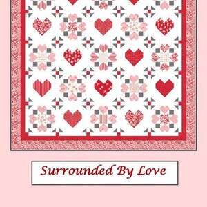May include: A red and white quilt with a heart and floral pattern. The quilt features a repeating design of red hearts and floral shapes on a white background, framed by a red border. The text "Sew-N-Quilt" and "Surrounded By Love" are also visible.