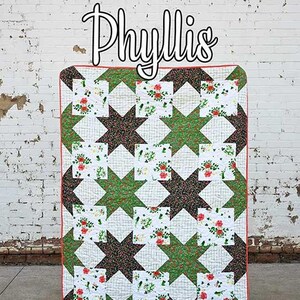May include: A handmade quilt with a star pattern in green, brown, and floral fabrics. The quilt has a red border and the word "Phyllis" in script. The Running Doe Quilts logo is at the bottom.