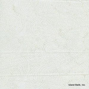 May include: Off-white fabric with a subtle pattern of small, light-colored dots arranged in swirling designs. The fabric has a slightly textured appearance and visible horizontal folds. The words "Island Batik, Inc." are in the bottom right corner.