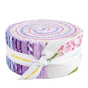 Puede incluir: Un rollo de tiras de tela en tonos morados, rosas y blancos, atado con una cinta blanca. La tela presenta diseños florales y estampados. La cinta lleva la inscripción "create colorfully".