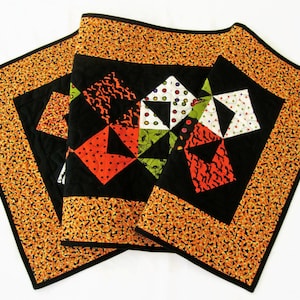 May include: Three black and orange Halloween table runners with a black center featuring a patchwork design of orange, white, green, and black fabric with geometric shapes.