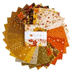 May include: A stack of square fabric swatches arranged in a circular fan pattern, featuring various autumn-themed prints in shades of orange, yellow, brown, and cream. A white paper band wraps around the center with the text "Beautiful".