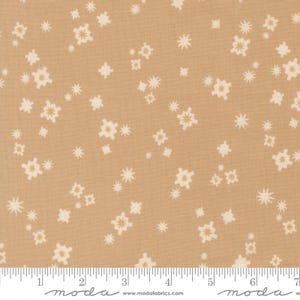 May include: Tan fabric with a repeating pattern of off-white starburst and floral shapes. The fabric is measured with a ruler in inches, showing a scale for size reference. The overall design is a neutral, versatile pattern suitable for various sewing projects.