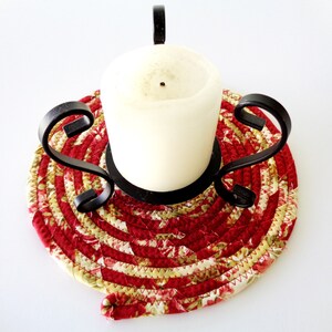 May include: A white candle sits on a red and cream floral fabric candle holder with a black metal base.