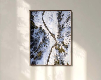 May include: A framed aerial photograph of a snow-covered landscape. A winding river cuts through the center, flanked by snow-covered banks and evergreen trees. The photograph is in a brown wooden frame.