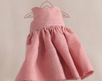 May include: A pink linen dress hanging on a hanger. The dress has a simple design with a gathered skirt and a straight neckline.