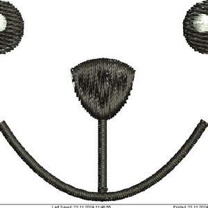 Könnte beinhalten: Nahaufnahme eines gestickten Designs mit einem Bärengesicht. Zwei dunkelgraue Kreise mit weißen Zentren stellen die Augen dar, eine schildförmige Nase und ein gebogener Mund. Auf weißem Hintergrund.