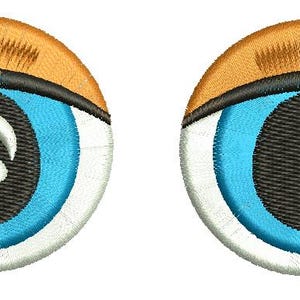 Op de afbeelding: Twee geborduurde oogpatches. Elke patch heeft een blauwe iris, een zwarte pupil, witte highlights en een gebogen zwarte bovenste wimperlijn. Het bovenste deel van elk oog is bruin, met zwarte wimpers.