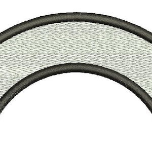 May include: A curved, embroidered patch. It features a light grey, textured interior and a dark grey border. The patch has a semi-circular shape, with a slightly curved top and bottom edge. The design is simple and clean.