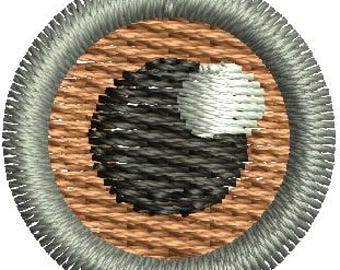 May include: Embroidered circular patch featuring a stylized eye design. The eye's pupil is black and gray, with a white highlight. The eye is set against a tan background, surrounded by a silver-gray border.