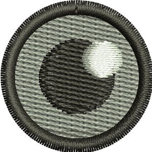 Puede incluir: Un parche para el ojo bordado en blanco y negro sobre un fondo gris. El parche para el ojo es circular y tiene un borde cosido.