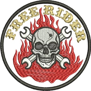 May include: A circular embroidered patch featuring a white skull wearing round glasses, positioned in front of two crossed silver wrenches and red flames. The text FREE RIDER is stitched in gold thread along the top edge, all bordered by black.
