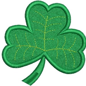 May include: A green embroidered shamrock with three heart-shaped leaves and a stem. The shamrock has yellow stitching details that outline the leaves and veins. The image is a close-up of the shamrock.
