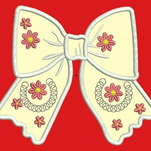 Può includere: Un fiocco bianco con fiori rosa e un design a ferro di cavallo argentato. Il fiocco è su uno sfondo rosso.