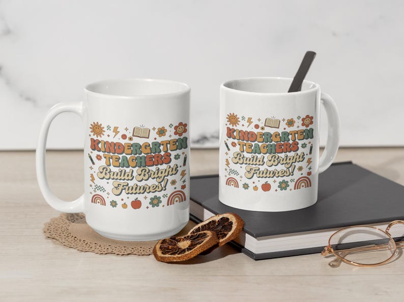 May include: Two white ceramic mugs with the text "KINDERGARTEN TEACHERS Build Bright Futures!" in a retro font. The mugs have a handle and are decorated with colorful illustrations of a sun, flowers, and rainbows. One mug has a spoon.