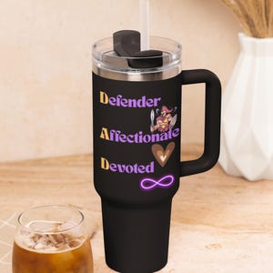 Op de afbeelding: Zwarte geïsoleerde beker met een handvat, doorzichtig deksel en rietje. De beker heeft de woorden "Defender, Affectionate, Devoted" in goud en paars, samen met een cartoon krijger en een oneindigheidssymbool.