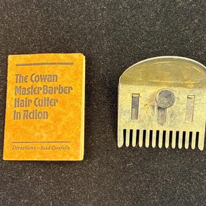 May include: An antique hair cutting tool and instruction booklet. The metal hair cutter is gold-toned with a comb-like edge. The booklet is orange with black text that reads "The Cowan Master Barber Hair Cutter In Action."