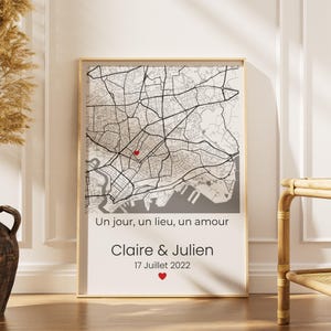 Puede incluir: Impresión enmarcada de un mapa de la ciudad con un diseño de mapa, con un corazón rojo que marca una ubicación. La impresión incluye el texto "Un jour, un lieu, un amour", los nombres "Claire & Julien" y la fecha "17 Juillet 2022".