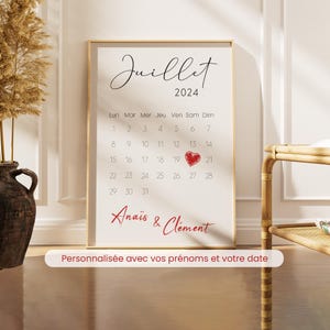 May include: A framed calendar print for July 2024, featuring a heart on the 21st. The names "Anaïs & Clément" are written in red script. The text "Personalized with your names and your date" is at the bottom.