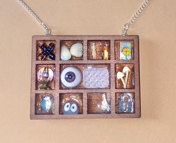 A tiny wearable curiosity cabinet packed with miniature oddities — crystal ball, eye, teeth, and more — genuinely handmade and one-of-a-kind.