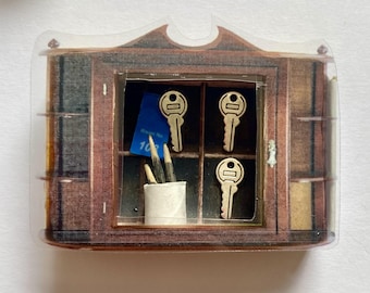 May include: A miniature wooden cabinet with a clear plastic cover featuring three metallic keys, a small white container holding two pointed wooden sticks, and a blue rectangular tag with the white text 108 printed on the surface.