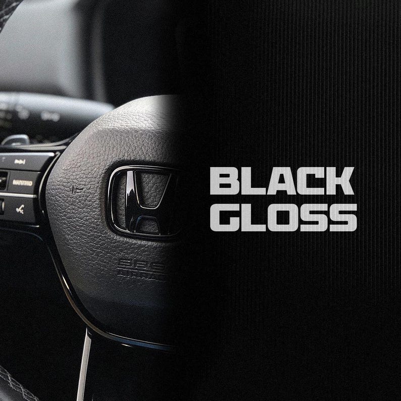May include: A black steering wheel with the Honda emblem, alongside the white text "BLACK GLOSS". The image is a product shot, possibly for a car accessory. The steering wheel is a prominent feature.