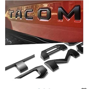 May include: Black plastic letters that spell out "TACOMA" for a vehicle. The letters are separate and ready to be applied to a vehicle.