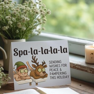 May include: A greeting card with the text "Spa-la-la-la-la" and a cartoon of an elf and a reindeer relaxing at a spa. The card also says "Sending wishes for peace & pampering this holiday". A lit candle and flowers are in the background.