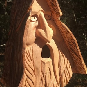May include: A wooden carving of a face with a long beard and a wide-open mouth. The carving is painted in shades of brown and has a rustic appearance.