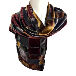May include: A velvet scarf with a patchwork design. The scarf features burgundy, gold, brown, and black colours. The scarf is draped over a white mannequin head.
