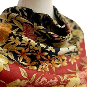 May include: A patterned scarf with a floral design. The scarf has a black background with yellow and orange flowers, and a red border with large yellow hibiscus flowers. The scarf is draped over a mannequin.