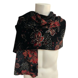 May include: A black velvet scarf featuring a repeating floral pattern in shades of red and gold, accented with small circular motifs. The fabric has a soft, textured appearance with a deep black background and vibrant red flower petals.