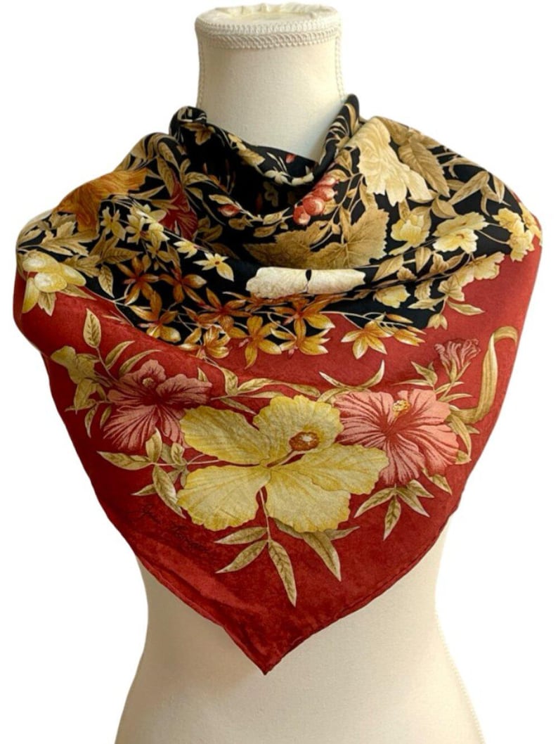 May include: A square silk scarf with a floral design. The scarf has a red border with large yellow and pink flowers. The centre of the scarf is black with a pattern of yellow, brown, and red flowers.