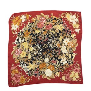 May include: A square silk scarf with a floral pattern. The scarf has a black centre with a vibrant arrangement of yellow, orange, pink, and white flowers. A red border frames the floral pattern. A fashion accessory.