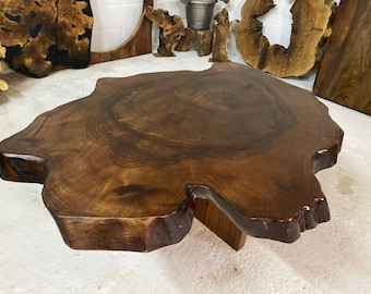 May include: A large, round, wooden coffee table with a natural, live edge design. The table top is a rich brown color and has a smooth, polished finish. The table is supported by a single, sturdy wooden leg.
