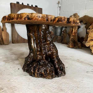 May include: A rustic wooden table with a live edge top and a tree trunk base. The table is stained a dark brown colour and has a natural, organic look.