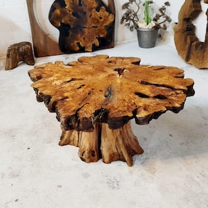 May include: A rustic wooden coffee table with a large, round, natural wood top and a thick, irregular base. The table has a unique, organic shape and a warm, natural finish.