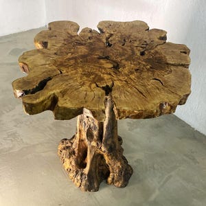 May include: A handcrafted wooden side table with a natural, irregular top and a light brown finish. The table is supported by a textured, dark brown base. The design highlights the natural grain and shape of the wood. The table's dimensions are approximately 76 cm in height.