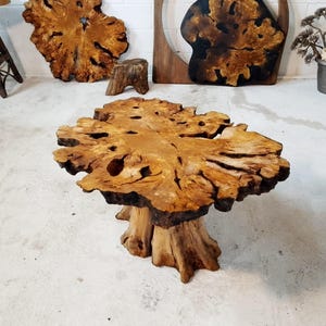 May include: A large, natural wood coffee table with a unique, irregular shape and a thick, sturdy base. The table top has a rich, brown color and a natural, rustic finish.