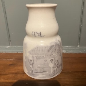 May include: White ceramic jar with a bulbous base and a narrow neck. The jar features a blue and white illustration of a market scene with the text "Lucknow Chutney". The jar has the initials "RT" in blue.
