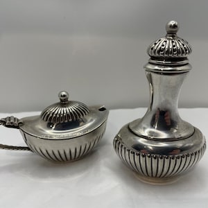 May include: Two antique silver serving pieces. One is a small, lidded creamer with a handle. The other is a tall, lidded container with a bulbous base and a decorative top. Both pieces have a ribbed design.