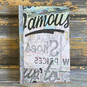 May include: A rectangular book with a map design. The cover features the word "Famous" in large black script, with additional text and map details. The background is a mix of green, blue, and white map sections.