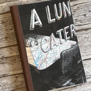 May include: A rectangular notebook with a brown spine and a cover featuring a black and white map graphic overlaid with the text A LUN ATER in large white letters. The map displays various road routes and geographic locations in detail.